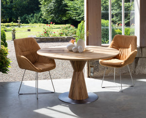 Runder Massivholztisch RADON aus Eiche von Scholtissek in wohnlichem Ambiente mit hellen Polsterstühlen und modernem Kunst-Interieur im Hintergrund.
