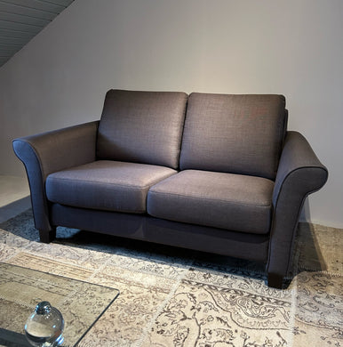 Frontansicht des Schröno Sofa Individual in braunviolettem JAB Anstoetz Stoff Vito 55 auf Teppich mit Glas-Couchtisch