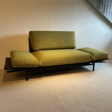 Laden Sie das Bild in den Galerie-Viewer, Dema Rataplan Sofa vollständig zur Liegefläche umgeklappt, beide Armlehnen flach gestellt, Funktion als Daybed demonstriert, schwarzes Untergestell und grüner Polsterstoff.
