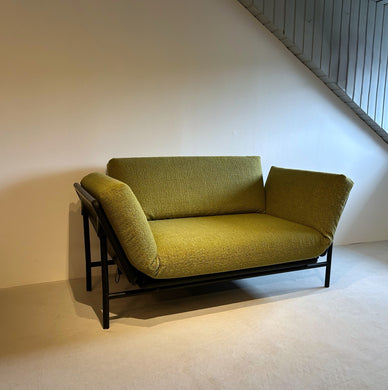 Grünes Dema Rataplan 2-Sitzer-Sofa in aufrechter Position mit beiden Armlehnen hochgeklappt, schwarzes Metallgestell, Ausstellungsstück im Neuzustand vor weißer Wand unter Dachschräge.