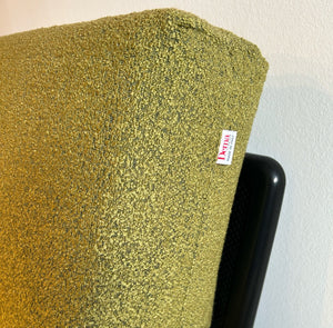 Detailaufnahme der grünen Rückenlehne des Rataplan Sofas mit sichtbarem Dema-Etikett, feiner Bouclé-Stoff in grün und schwarzer Metallrahmen im Hintergrund.