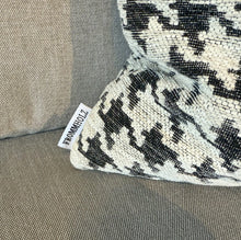 Laden Sie das Bild in den Galerie-Viewer, Nahaufnahme des Hahnentritt-Kissens mit Frommholz-Label auf dem grauen Sofa
