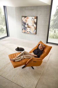 Nolte Lounger Miami in vollständiger Herz-Waage-Position, orangefarbenes Nappaleder, Frau entspannt liegend – ergonomischer Komfort in modernem Interieur.