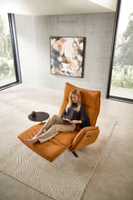 Laden Sie das Bild in den Galerie-Viewer, Relaxsessel Miami von Nolte in Relaxposition mit Frau beim Lesen – motorisch verstellbar mit Fußstütze, auf hell gemustertem Teppich in architektonischem Wohnraum.
