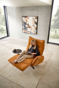 Relaxsessel Miami von Nolte in Relaxposition mit Frau beim Lesen – motorisch verstellbar mit Fußstütze, auf hell gemustertem Teppich in architektonischem Wohnraum.