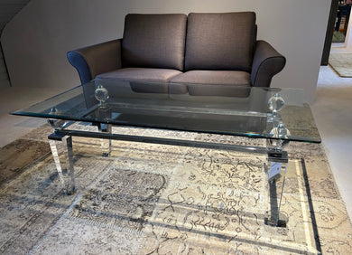 Eleganter Couchtisch aus Acryl und Glas von Kuatre, Ausstellungsstück auf Designteppich vor Frontansicht des Schröno Sofa Individual in braunviolettem JAB Anstoetz Stoff Vito 55 